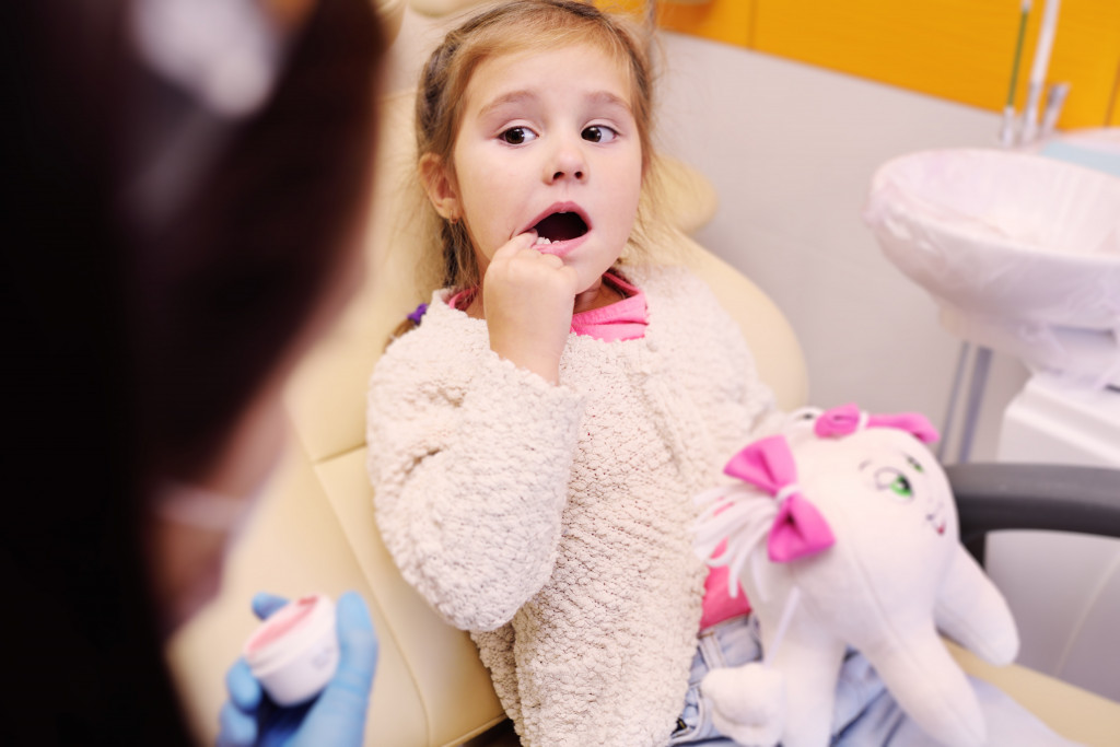 little girl point at teeth while sitting in dentist chair