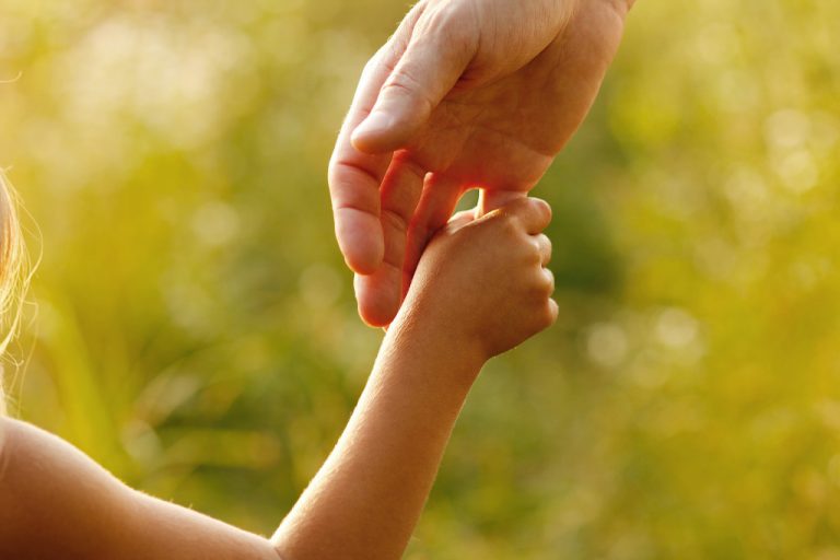 A close-up of a child holding the finger of her father, symbolizing trust