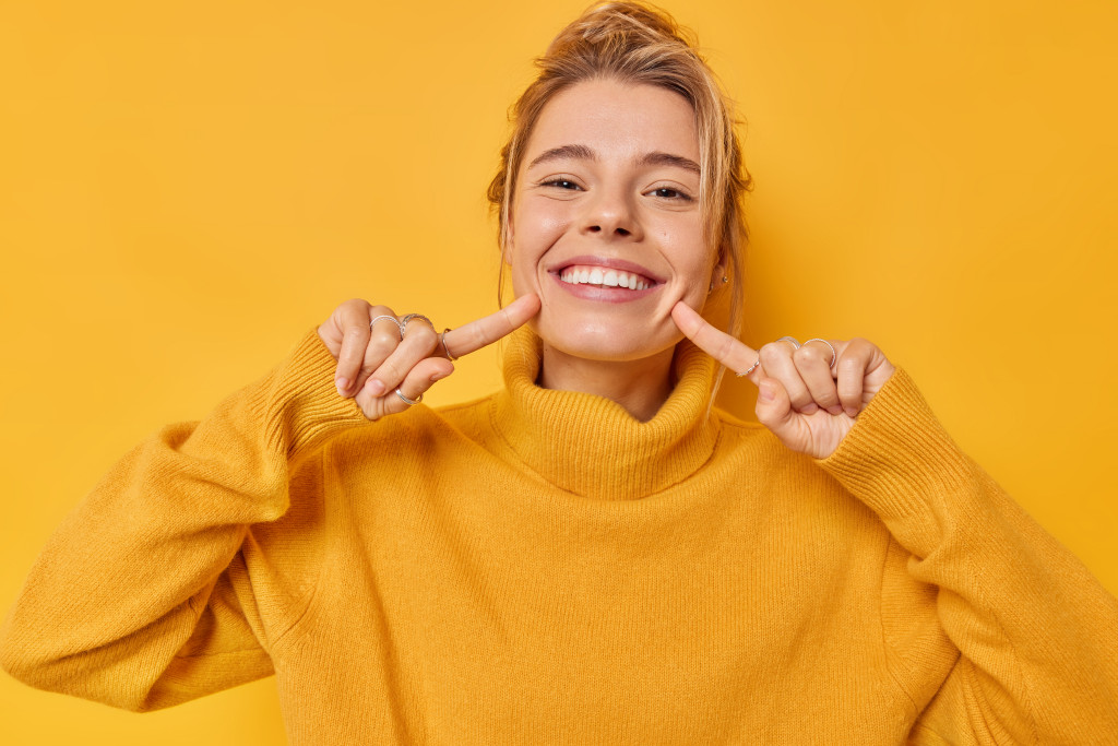 A woman smiles with her fingers pointed at her teeth