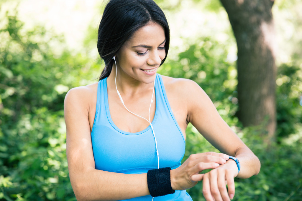 a smiling woman in headphones using a fitness tracker