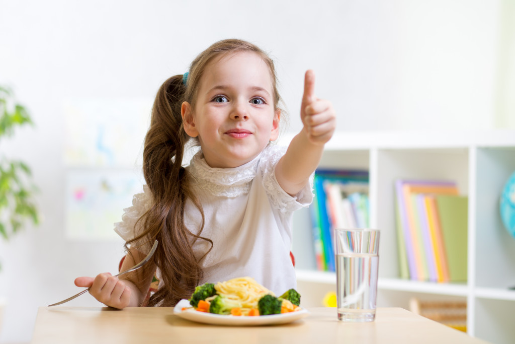 a young girl eating veggies while showing thumbs up