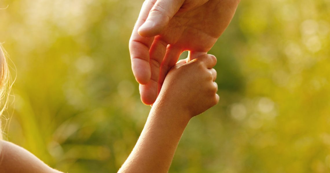 A close-up of a child holding the finger of her father, symbolizing trust